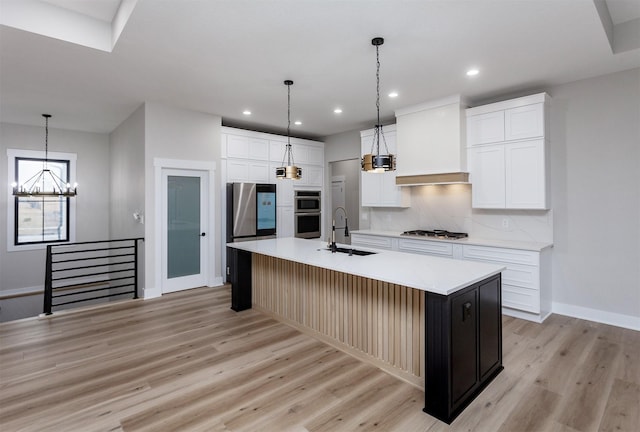 kitchen with stainless steel appliances, tasteful backsplash, light wood-style flooring, a sink, and premium range hood