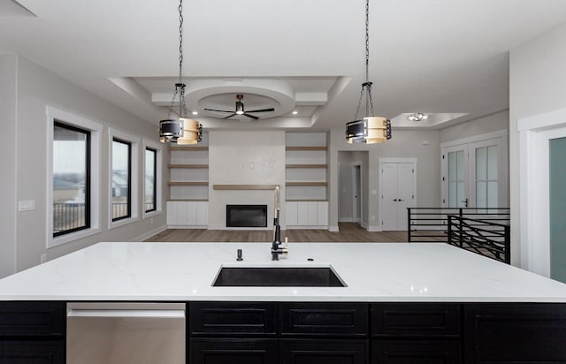 kitchen with a fireplace, stainless steel dishwasher, open floor plan, a sink, and dark cabinets