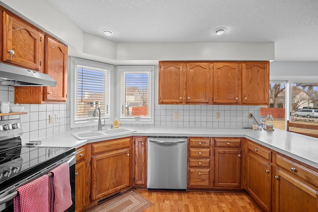 kitchen with light countertops, a textured ceiling, under cabinet range hood, appliances with stainless steel finishes, and a sink