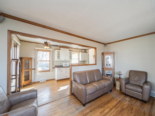 living area with light wood finished floors, baseboards, visible vents, and crown molding