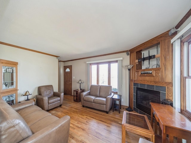 living area featuring light wood finished floors, crown molding, and a tiled fireplace