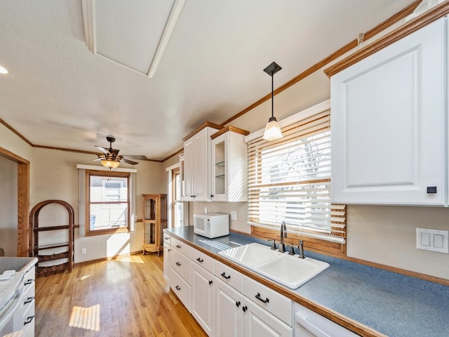 kitchen with light wood finished floors, white microwave, ornamental molding, white cabinetry, and a sink