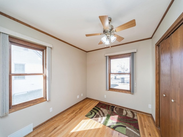 unfurnished bedroom with crown molding, multiple windows, visible vents, and light wood-style floors