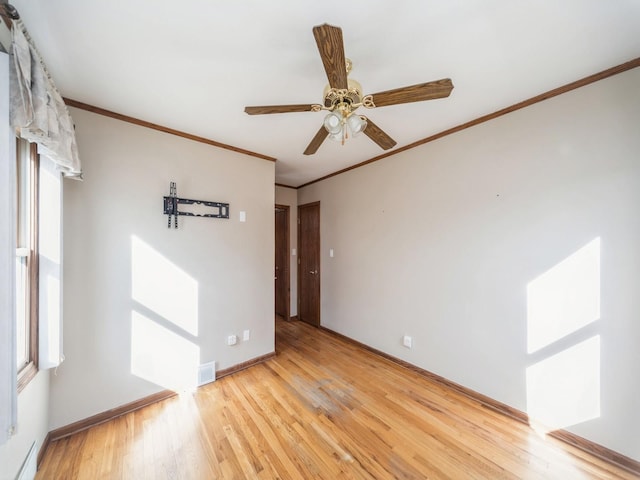 empty room featuring crown molding, visible vents, light wood-style flooring, a ceiling fan, and baseboards