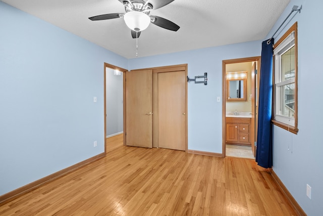 unfurnished bedroom featuring light wood finished floors, a closet, ensuite bathroom, a ceiling fan, and baseboards