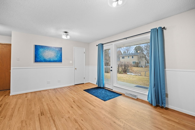 doorway to outside featuring a textured ceiling, wainscoting, wood finished floors, and visible vents