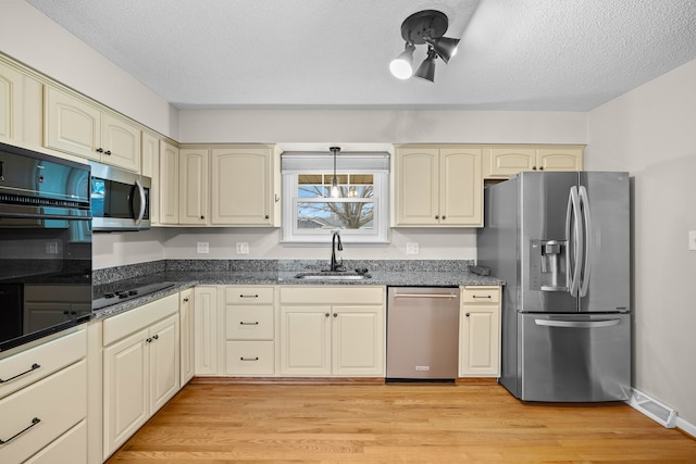 kitchen with black appliances, cream cabinets, a sink, and visible vents