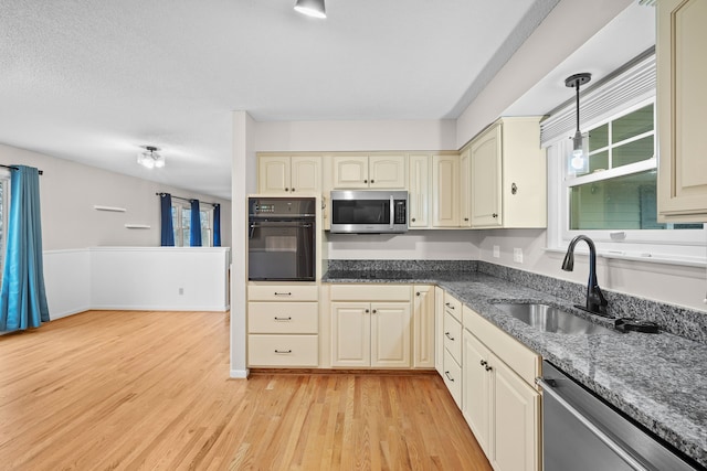 kitchen featuring hanging light fixtures, cream cabinets, appliances with stainless steel finishes, a sink, and light wood-type flooring