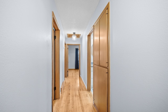 hall with light wood-type flooring, a textured ceiling, and baseboards