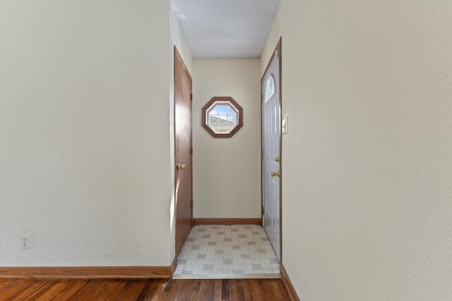 hall featuring a textured ceiling, baseboards, and wood finished floors