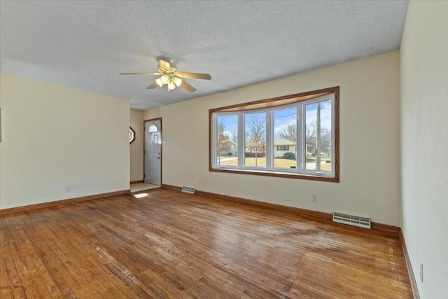 empty room with visible vents, hardwood / wood-style floors, a ceiling fan, a textured ceiling, and baseboards