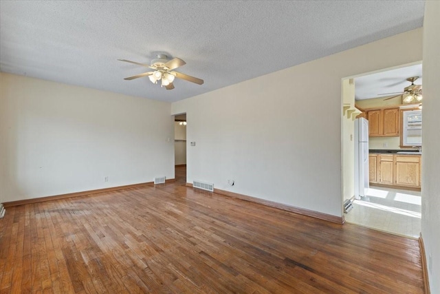 unfurnished room featuring a ceiling fan, wood-type flooring, visible vents, and baseboards