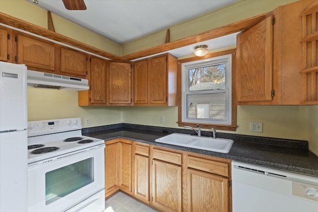 kitchen with white appliances, brown cabinetry, dark countertops, under cabinet range hood, and a sink