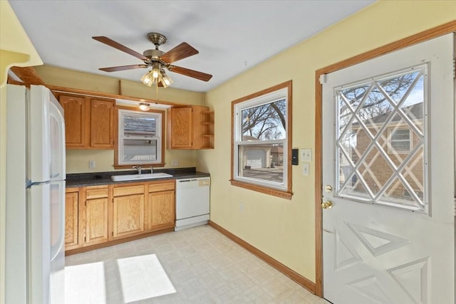 kitchen featuring white appliances, baseboards, dark countertops, light floors, and a sink