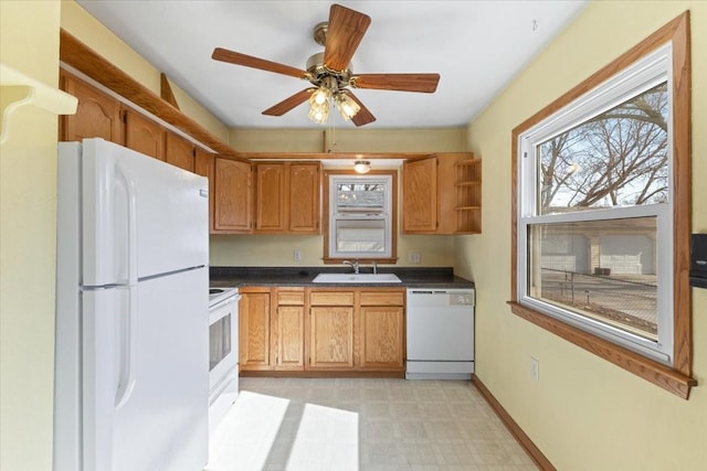 kitchen featuring light floors, dark countertops, a sink, white appliances, and baseboards