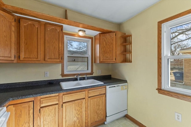 kitchen with light floors, dark countertops, brown cabinetry, white dishwasher, and a sink