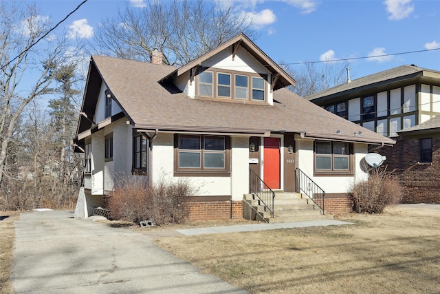 view of front facade with entry steps, roof with shingles, a chimney, and stucco siding