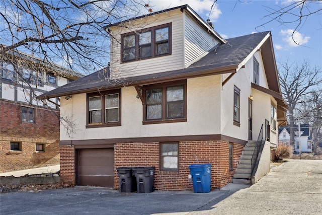 view of front of home featuring a garage, brick siding, a shingled roof, aphalt driveway, and stucco siding