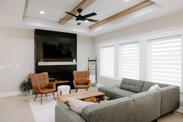 living room featuring a large fireplace, a tray ceiling, recessed lighting, and baseboards