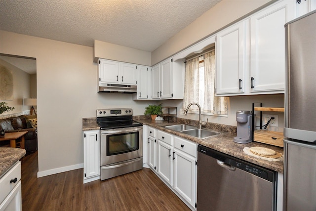 kitchen featuring dark wood finished floors, appliances with stainless steel finishes, under cabinet range hood, white cabinetry, and a sink