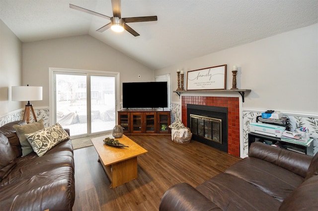 living room with vaulted ceiling, ceiling fan, a tiled fireplace, and wood finished floors