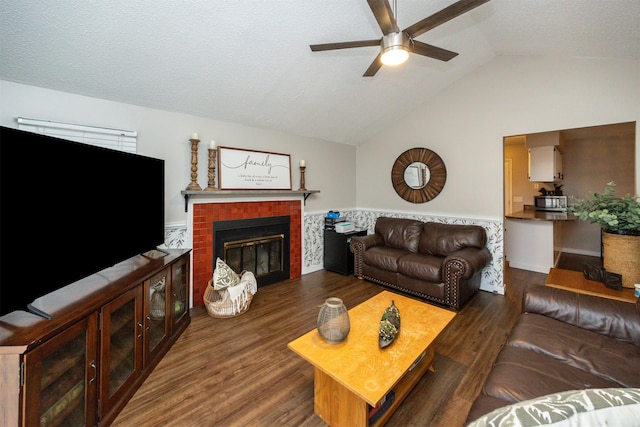 living area featuring a brick fireplace, a textured ceiling, vaulted ceiling, and wood finished floors