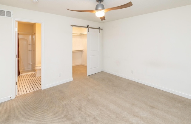 unfurnished bedroom featuring a barn door, visible vents, carpet, a spacious closet, and a closet