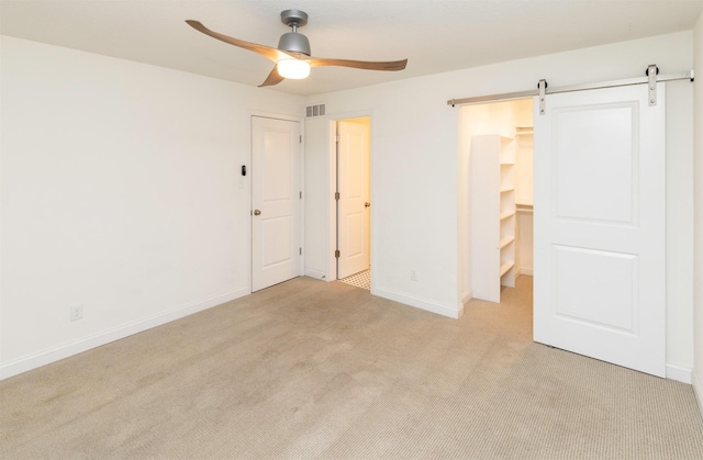 unfurnished bedroom featuring ceiling fan, a barn door, light carpet, baseboards, and a walk in closet