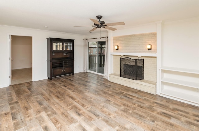 unfurnished living room featuring ornamental molding, a brick fireplace, ceiling fan, and wood finished floors