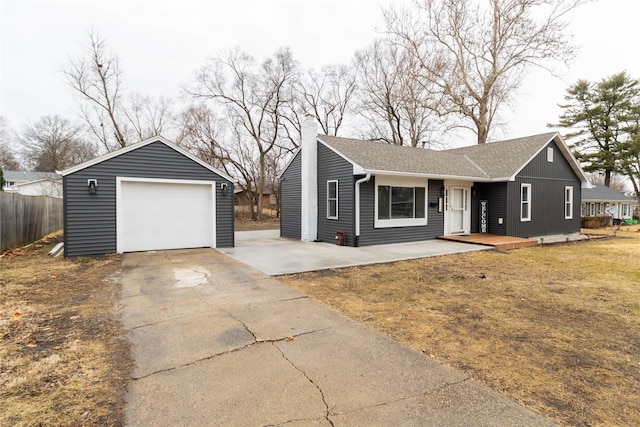 single story home featuring driveway, a garage, a shingled roof, an outdoor structure, and a front yard