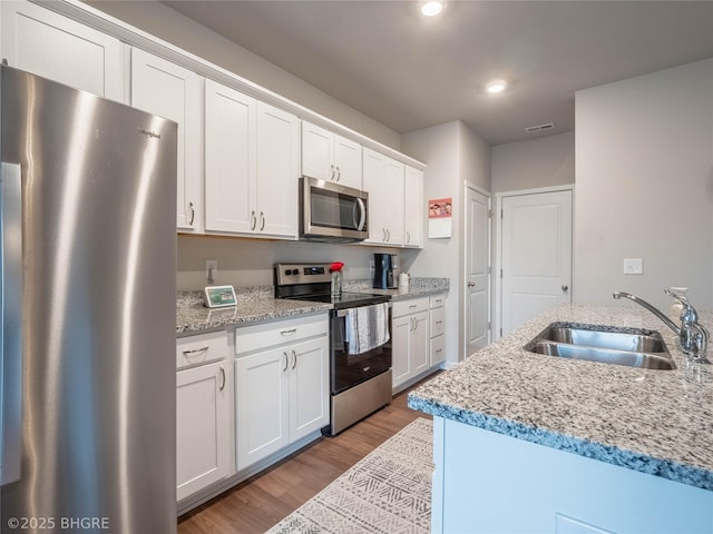 kitchen featuring light wood-style flooring, appliances with stainless steel finishes, white cabinets, a sink, and light stone countertops