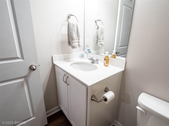 half bath with a textured wall, vanity, and toilet