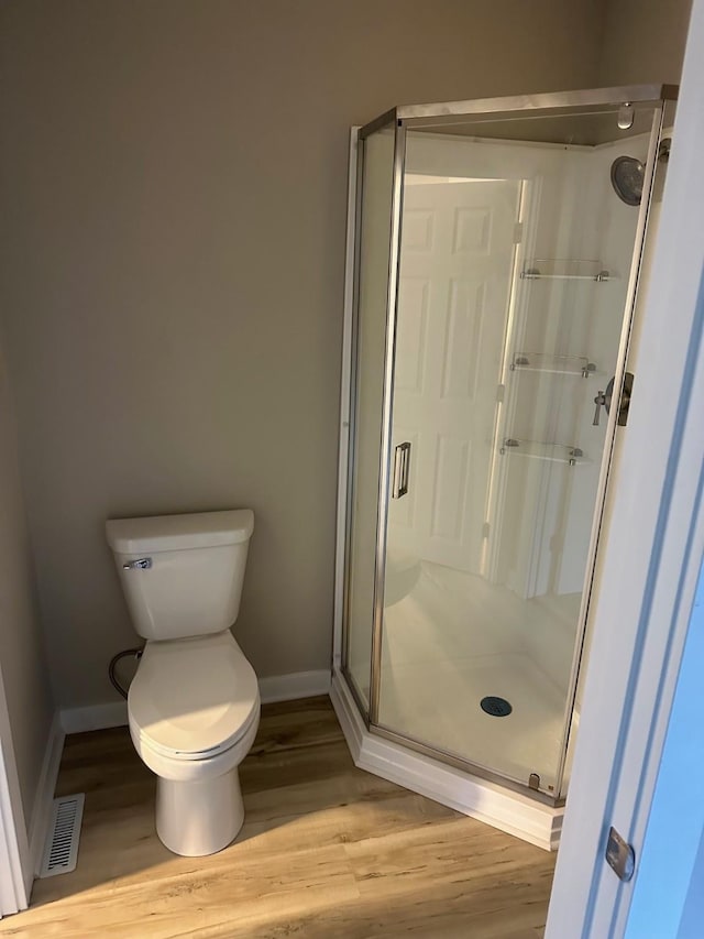 bathroom featuring toilet, wood finished floors, visible vents, baseboards, and a shower stall