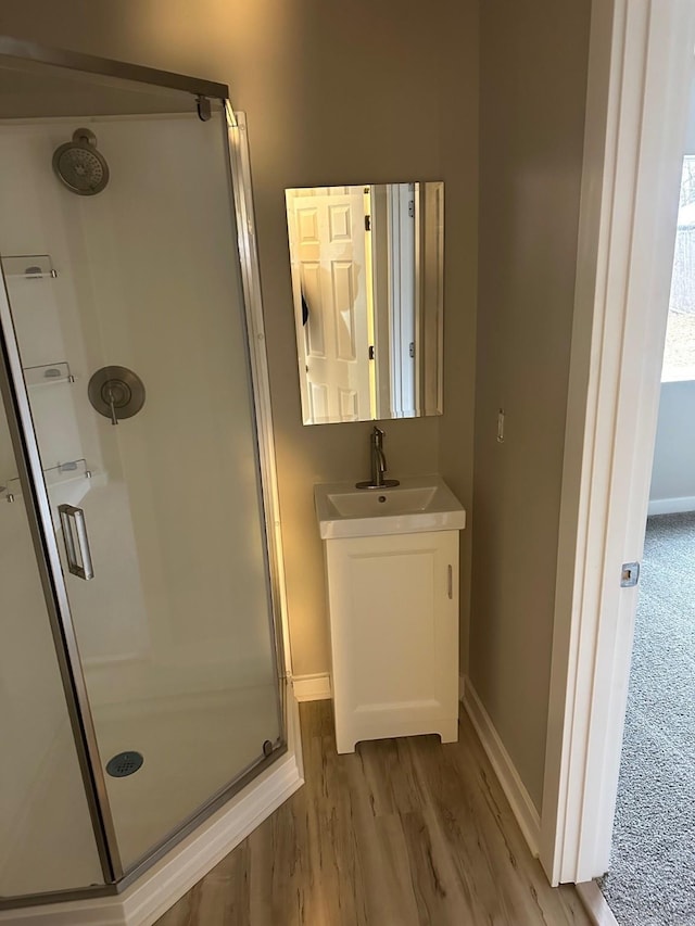 full bathroom featuring wood finished floors, a shower stall, vanity, and baseboards