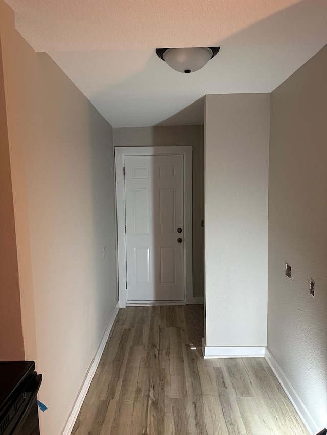 hall with a textured ceiling, light wood finished floors, and baseboards