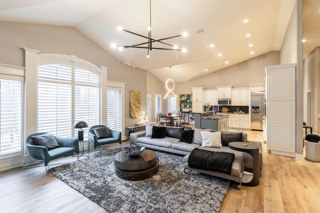 living room with a chandelier, plenty of natural light, high vaulted ceiling, and light wood finished floors