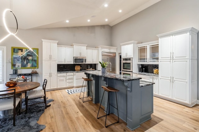 kitchen featuring a center island with sink, appliances with stainless steel finishes, light wood-style floors, white cabinets, and a kitchen breakfast bar