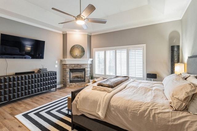 bedroom featuring crown molding, a tray ceiling, wood finished floors, and a stone fireplace