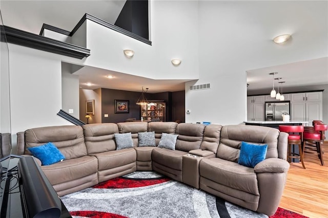 living area with light wood-style floors, visible vents, and a towering ceiling