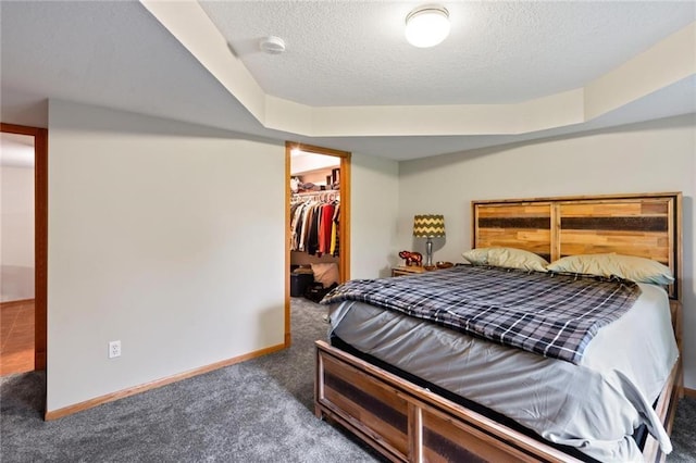 bedroom featuring a textured ceiling, carpet, a walk in closet, and baseboards