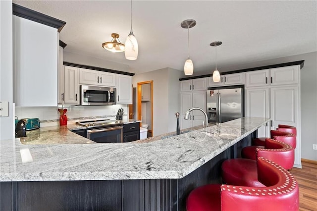 kitchen with light stone counters, stainless steel appliances, tasteful backsplash, light wood-type flooring, and a peninsula