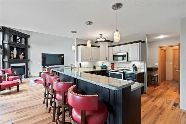 kitchen with appliances with stainless steel finishes, light stone counters, a breakfast bar area, a peninsula, and a lit fireplace