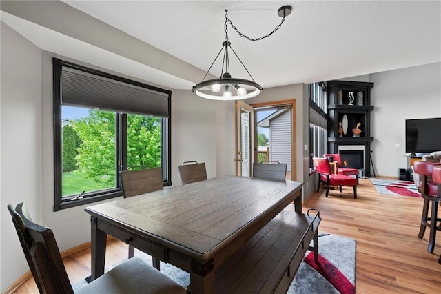 dining area featuring light wood-type flooring, plenty of natural light, a lit fireplace, and baseboards