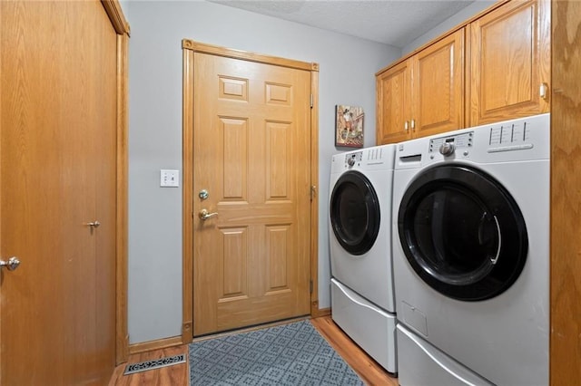 laundry room featuring light wood-style floors, cabinet space, washer and clothes dryer, and a textured ceiling