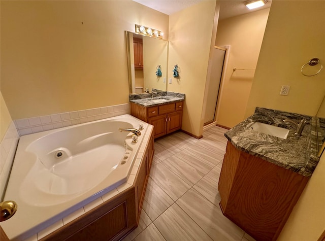 bathroom featuring a stall shower, a garden tub, two vanities, and a sink