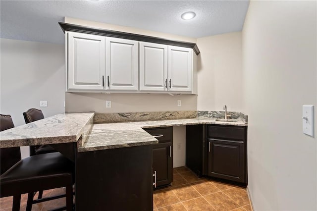 kitchen with light tile patterned floors, a peninsula, a kitchen bar, and white cabinetry