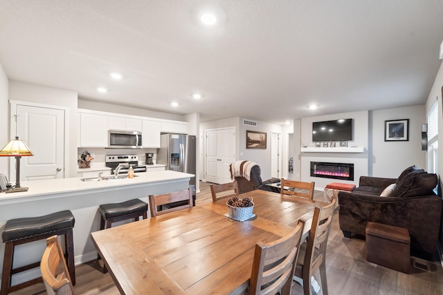 dining area with dark wood-type flooring, a glass covered fireplace, visible vents, and recessed lighting