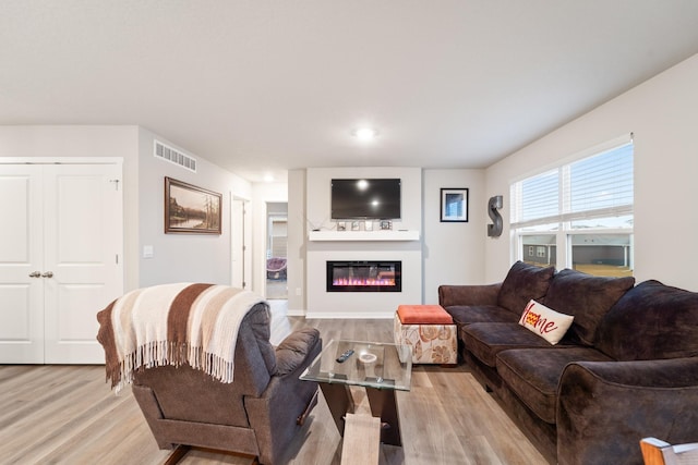 living area featuring light wood-type flooring, visible vents, and a glass covered fireplace