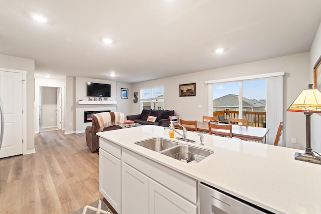 kitchen featuring dishwasher, a glass covered fireplace, open floor plan, light countertops, and a sink