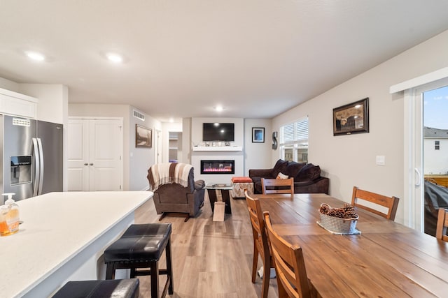 dining room with light wood-style flooring, a glass covered fireplace, visible vents, and recessed lighting